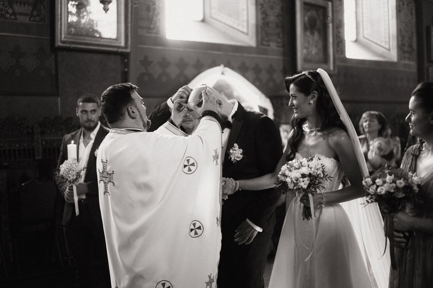 Black and white photo of a couple sharing a romantic moment during their wedding ceremony in a traditional church setting.