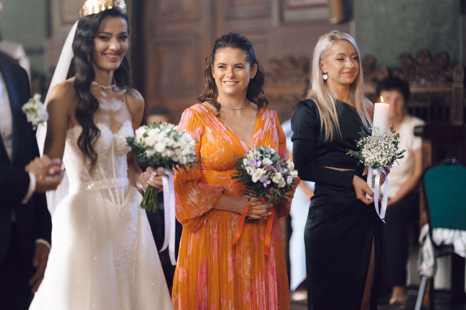 Wedding party members in orange bridesmaid dresses and white gowns pose together during celebration.