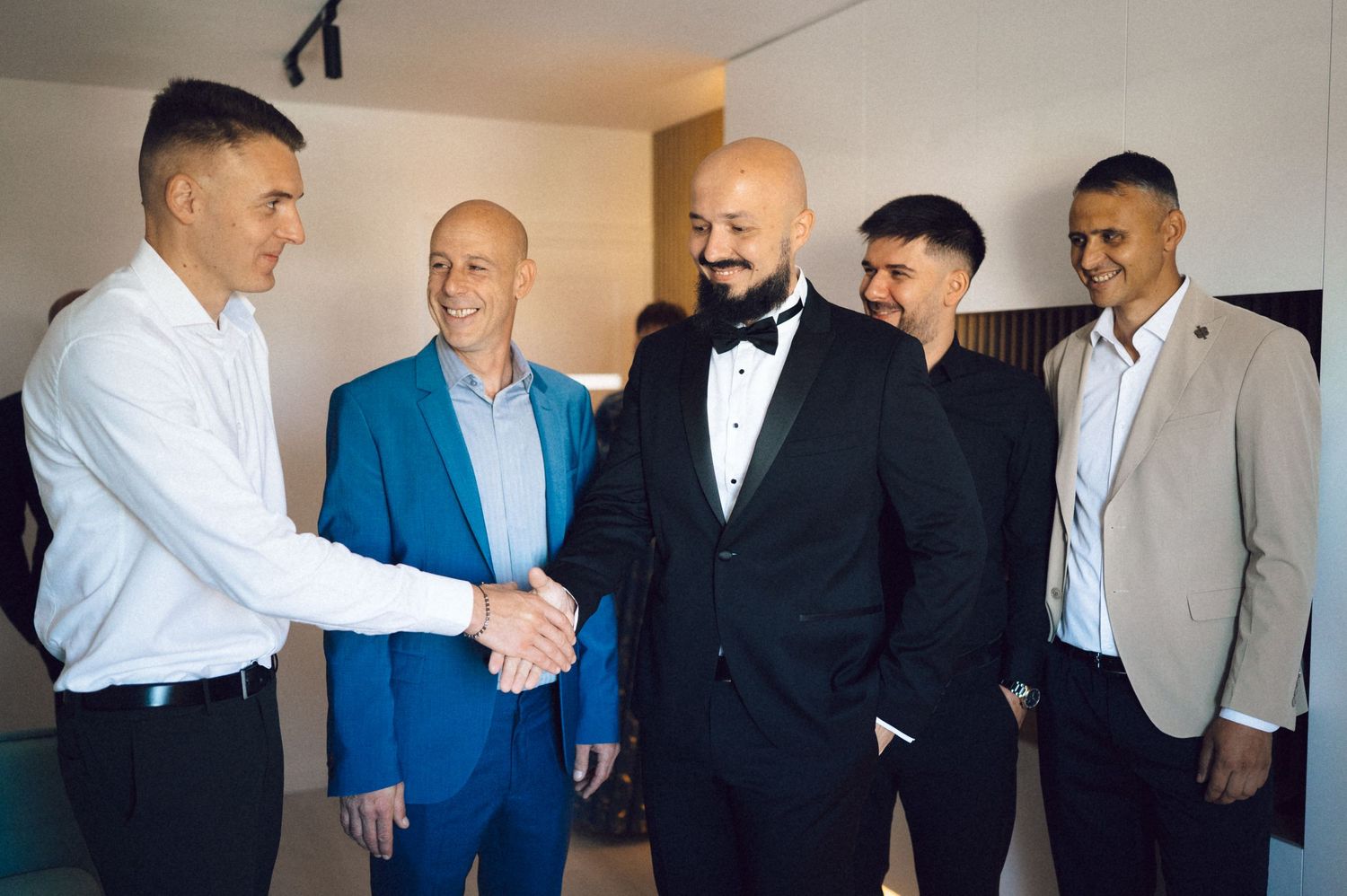 A group of men in formal attire gather together and shake hands before a special event.