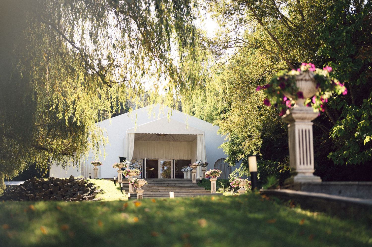 A white gazebo nestled among lush green trees and foliage in a tranquil garden setting.