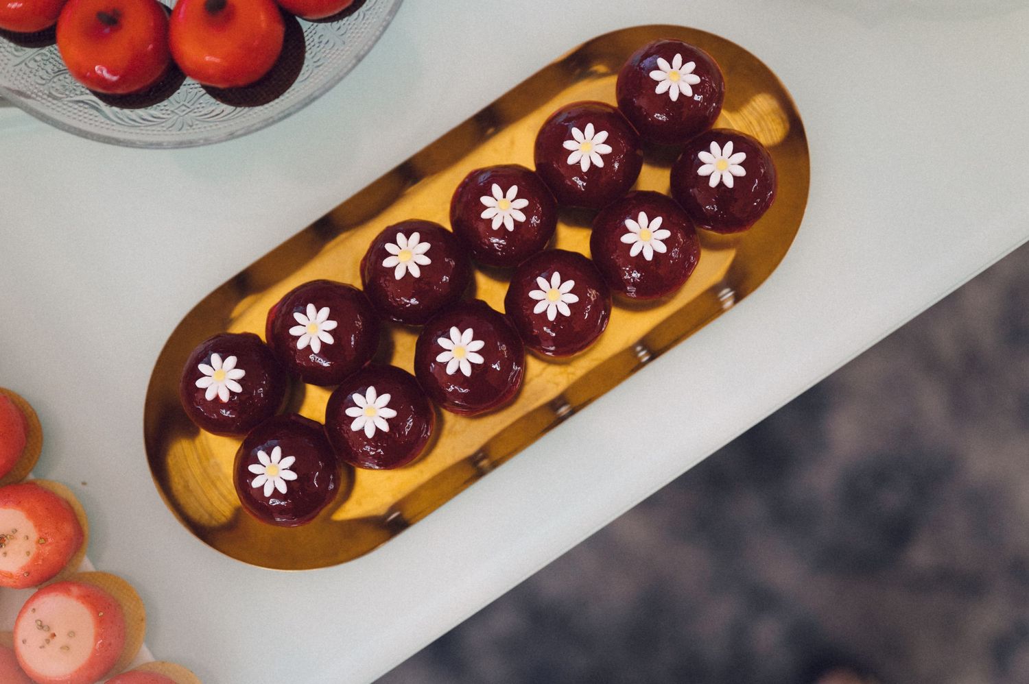 A chocolate eclair decorated with pink flower patterns sits on a golden serving plate.