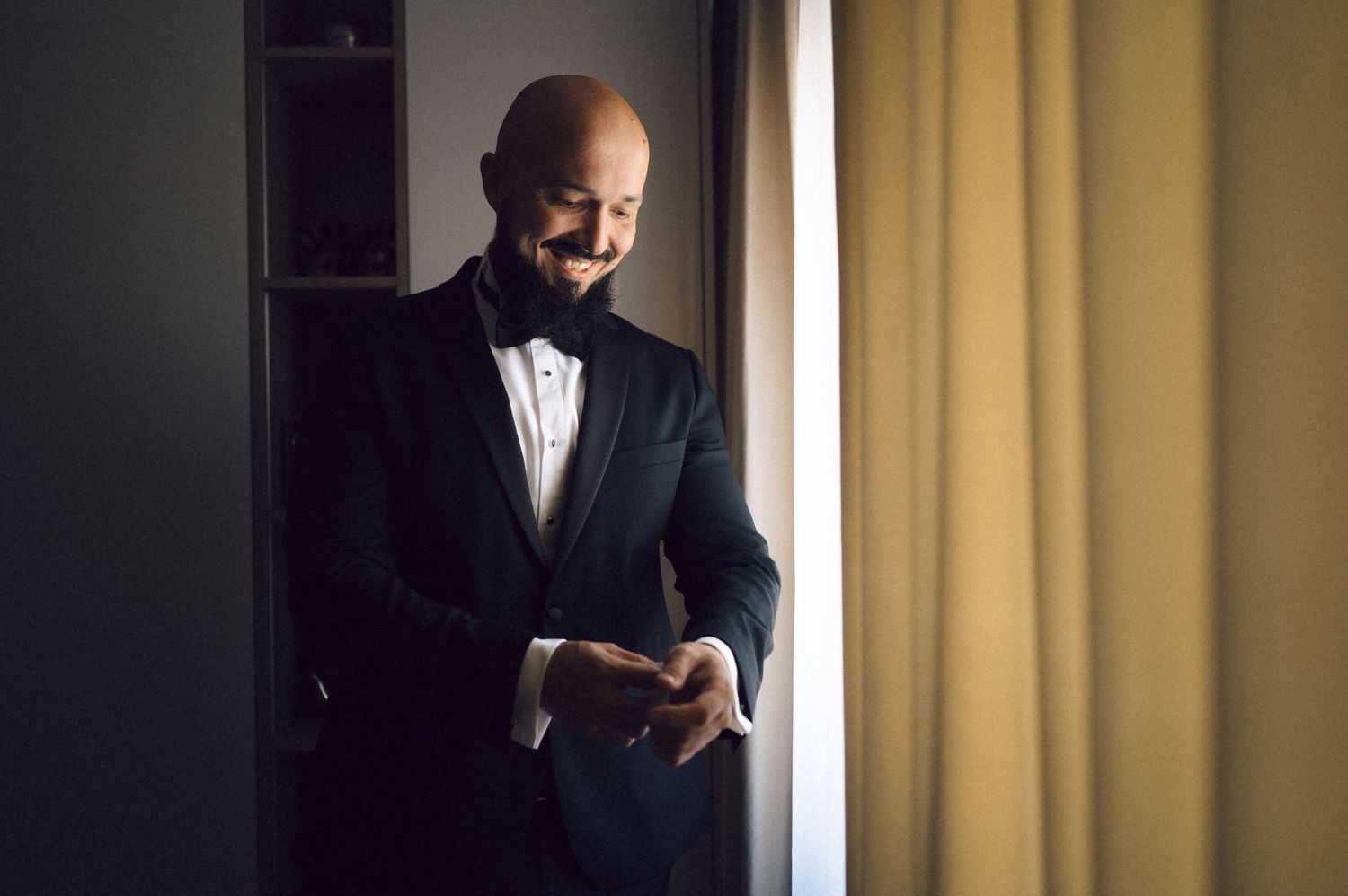 A person in a dark suit stands by a window with dramatic lighting casting shadows across their silhouette.