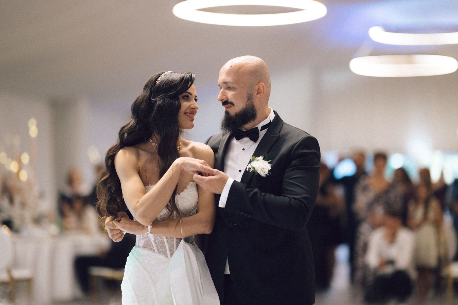 A couple shares an intimate dance at an elegant wedding reception with soft lighting and guests in the background.