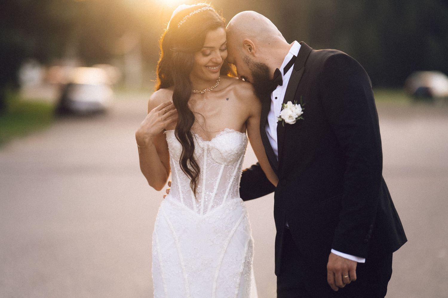 A happy bride and groom share a romantic moment outdoors in formal wedding attire.