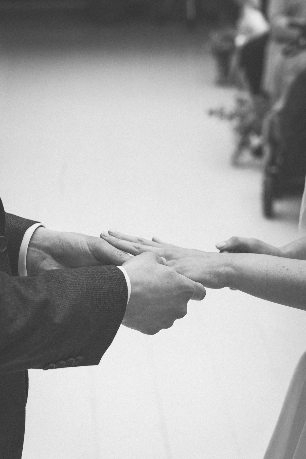 Black and white photo of a couple holding hands during a wedding ceremony ring exchange.