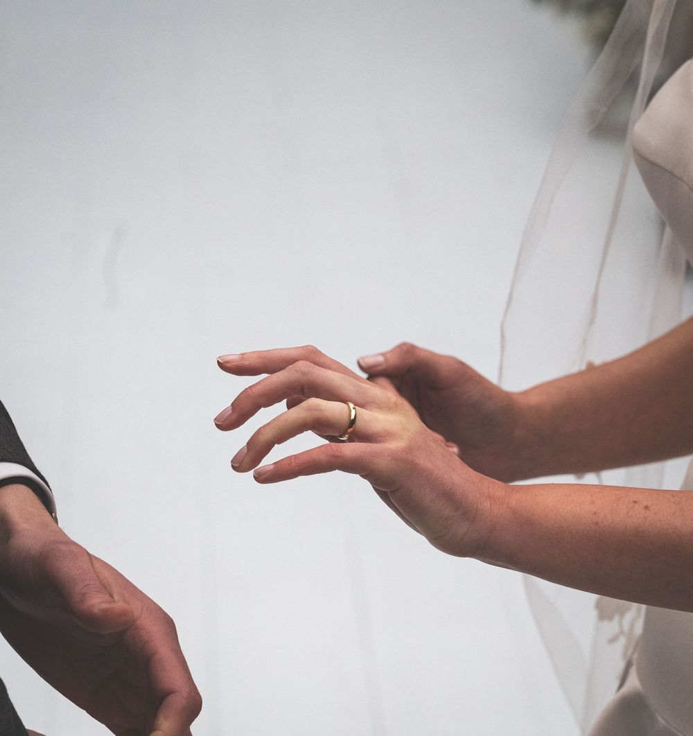 Close-up of bride and groom exchanging wedding rings during ceremony with veil in background.
