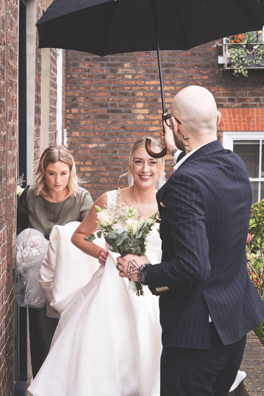 A couple shares a joyful moment under a brick archway in wedding attire.