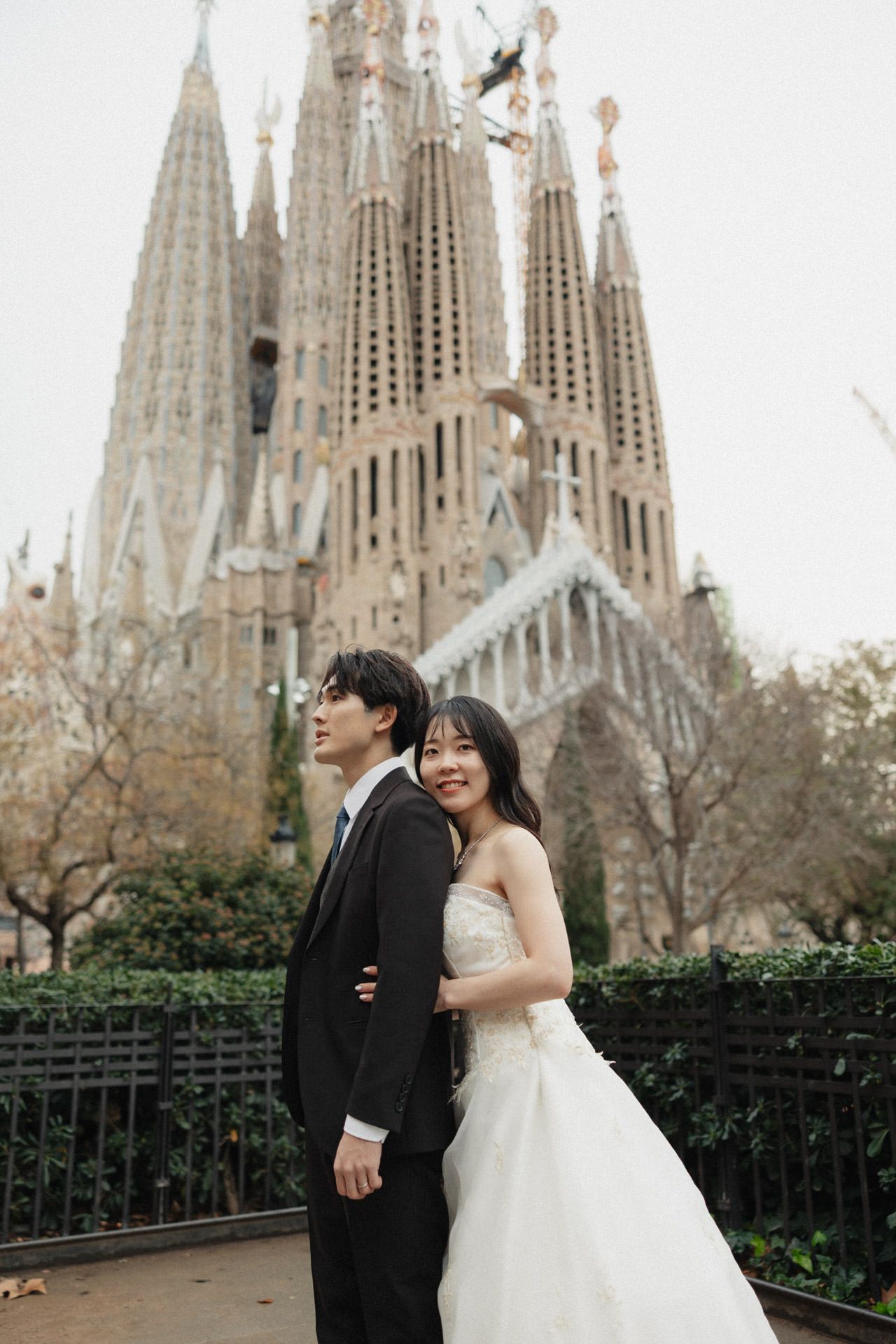 A couple poses for wedding photos in front of the iconic Sagrada Familia cathedral in Barcelona, Spain.