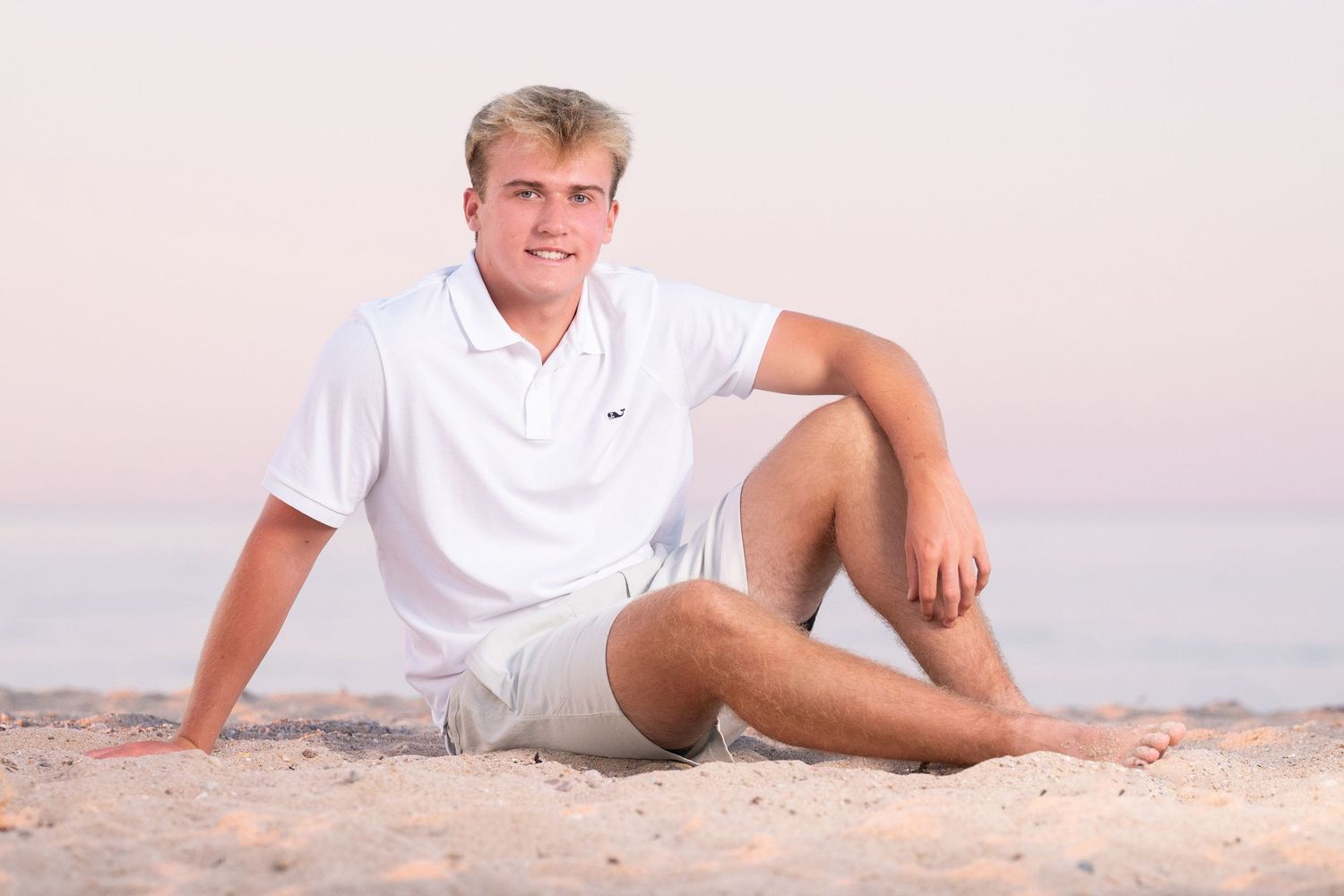 A person in white clothing poses on a sandy beach at sunset creating a relaxing coastal scene.