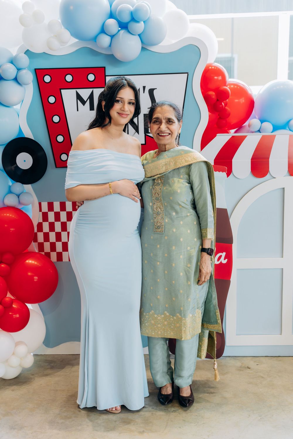 A baby shower celebration with blue and red balloon decorations and a checkered diner-themed backdrop.