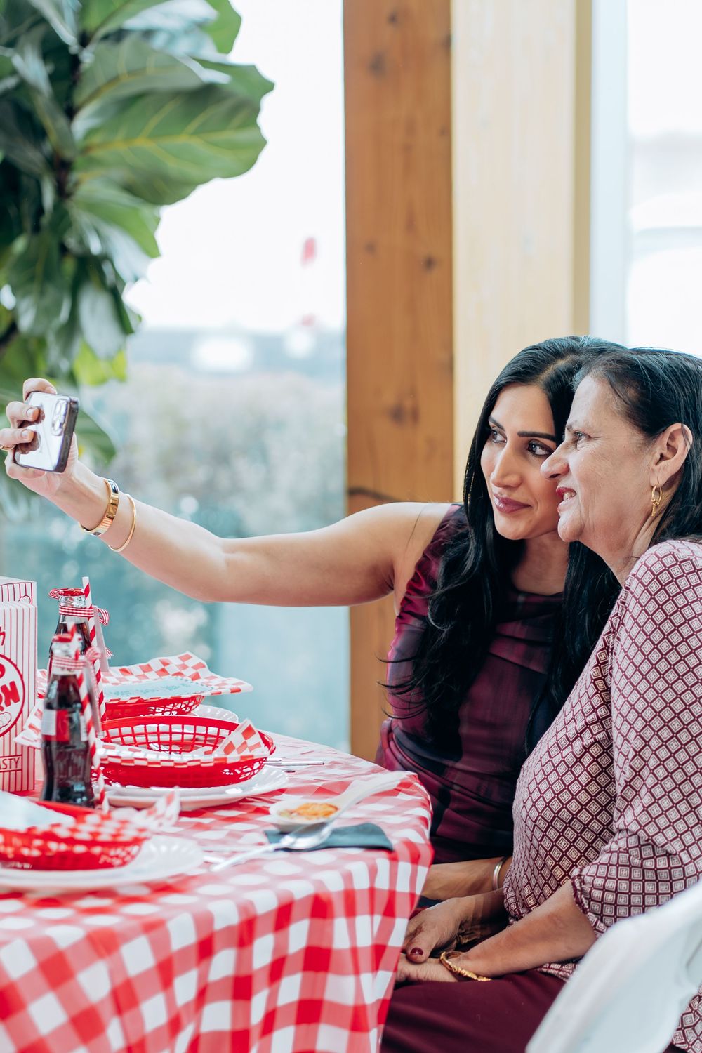 Friends enjoying conversation at a table with a red checkered tablecloth in a bright room.