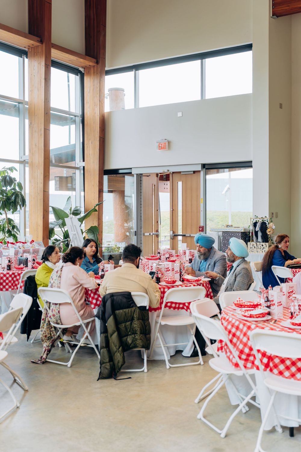 An event space set up with red and white checkered tablecloths and folding chairs in a bright room with windows.
