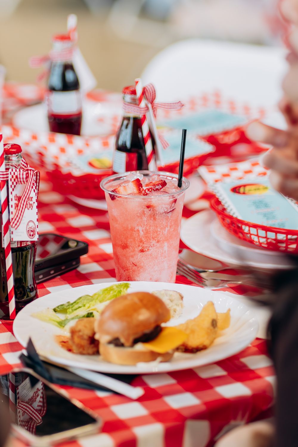 Retro diner themed party setup with red checkered tablecloths and classic soda bottles.