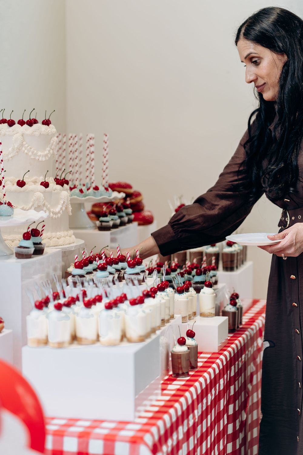 Dessert display featuring cupcakes topped with cherries on a red and white checkered tablecloth.