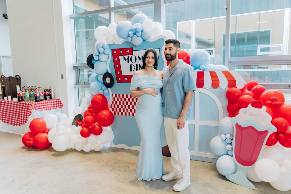 Red and blue balloon arch decorates a baby shower party space with soda shop themed decor and displays.