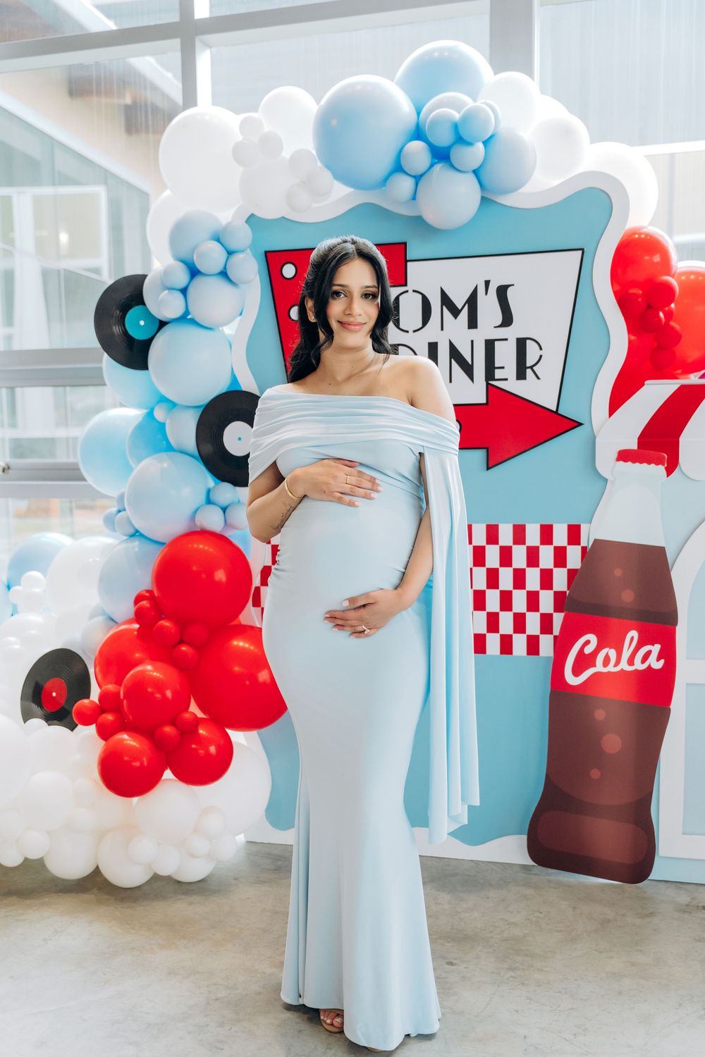 A maternity photo shoot with light blue balloons and red diner-themed decorations featuring a retro checkered pattern.
