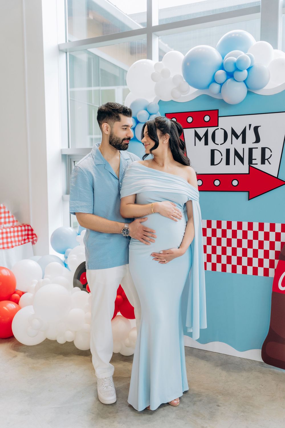 A series of maternity photos with a diner theme backdrop featuring blue and white balloon decorations.