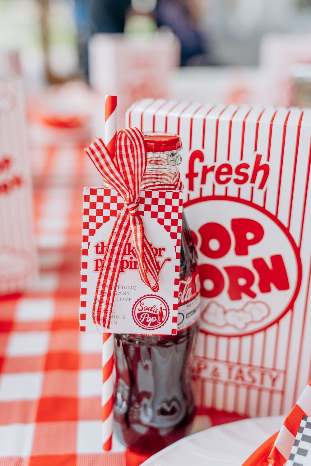 Red and white striped popcorn boxes decorated with checkered bows for a retro diner theme party.