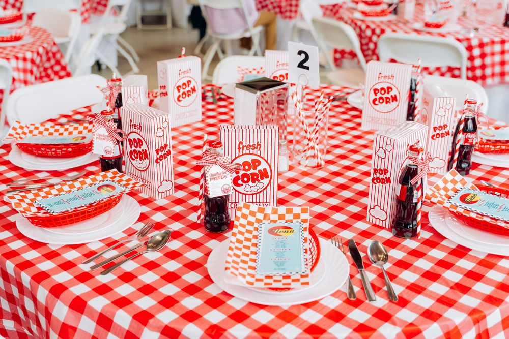 Red and white checkered tablecloth with vintage diner-style place settings and retro soda cups at a party table.