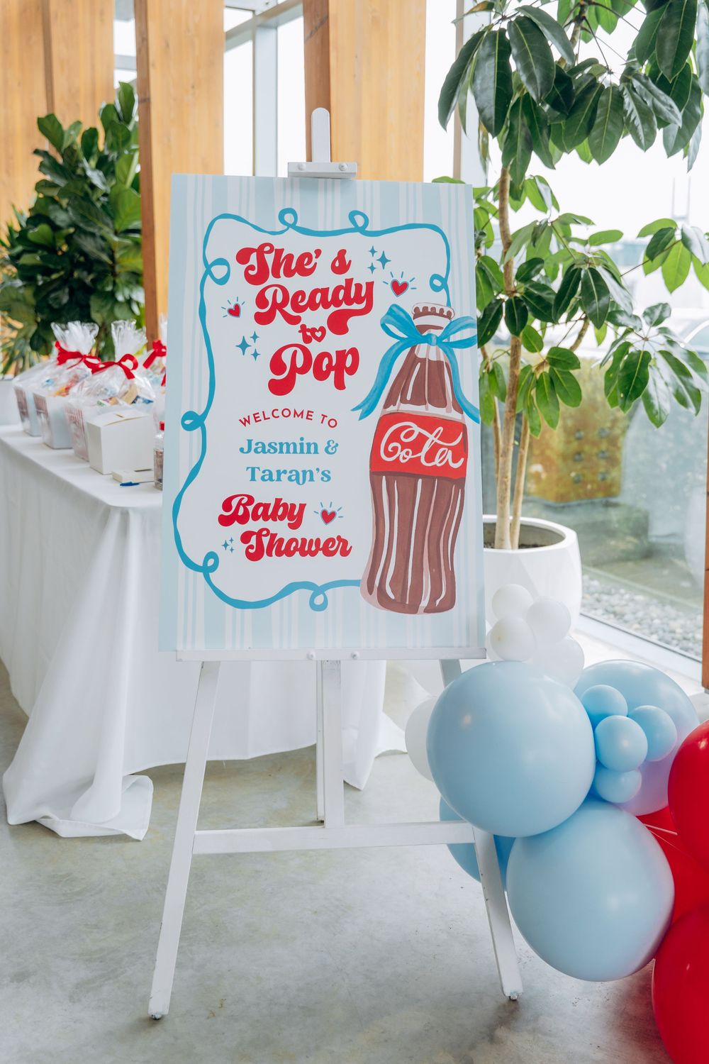Baby shower welcome sign featuring 'She's Ready to Pop' theme with soda pop design in red and blue colors.