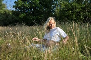 Pregnant blonde woman sitting peacefully in tall golden grass field outdoors.