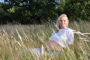 Pregnant blonde woman smiling while sitting in tall golden grass on sunny day.
