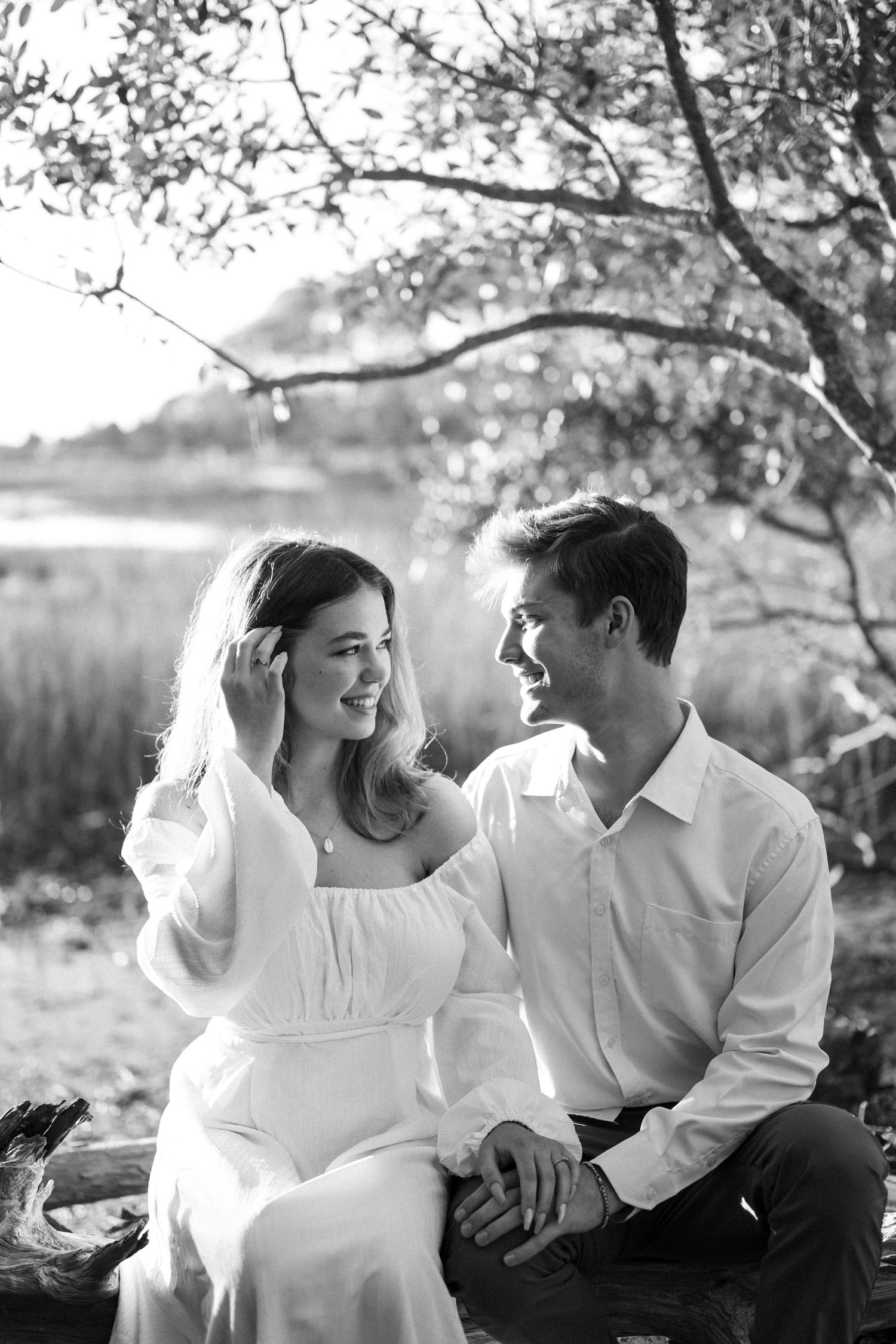 A couple embraces in a sunlit forest during golden hour, with tall pine trees creating a dreamy backdrop.