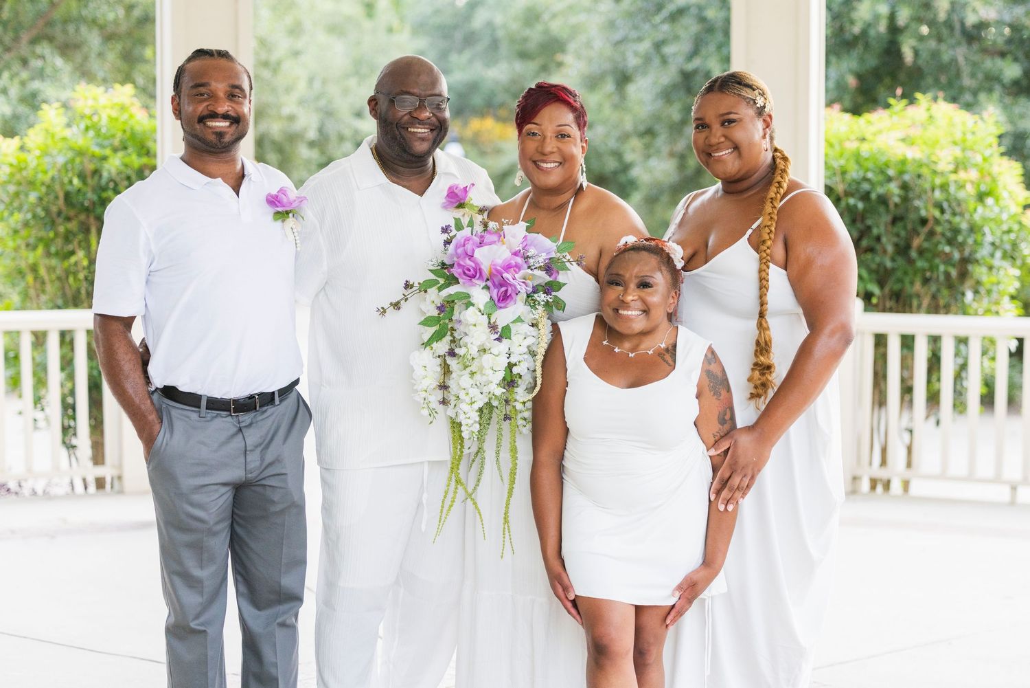 Wedding couple shares joyful moments together on a white gazebo porch with purple and white floral bouquet.