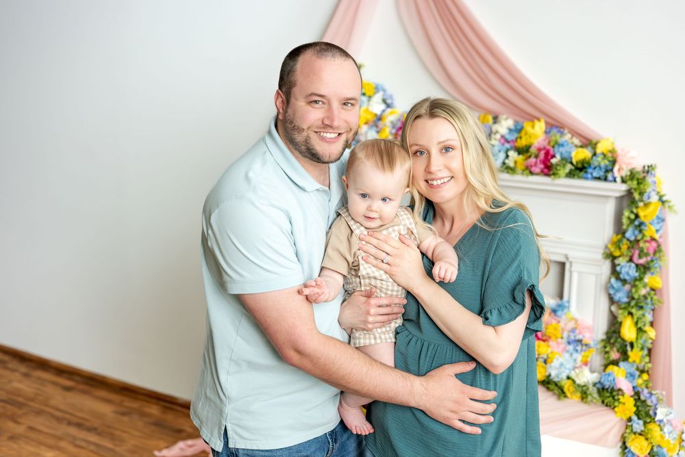 Happy family portrait with parents holding baby in floral decorated studio.