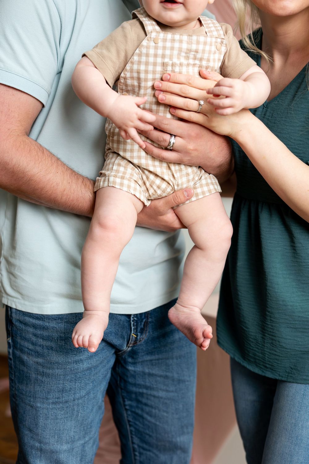 Parents holding smiling baby in checkered outfit in bright studio.