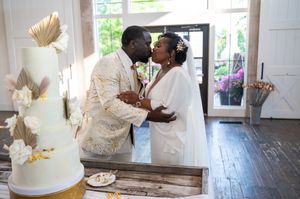 Bride and groom share a kiss beside a elegant white wedding cake during their reception ceremony.