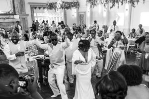 Black and white photo of wedding guests dancing joyfully at an elegant indoor wedding reception celebration.