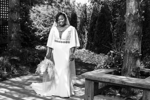 Black and white photo of a smiling bride in a white gown holding a bouquet in a sunlit garden.