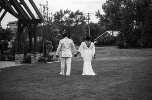 Black and white photo of a bride and groom holding hands walking across a lush green lawn at their outdoor wedding.