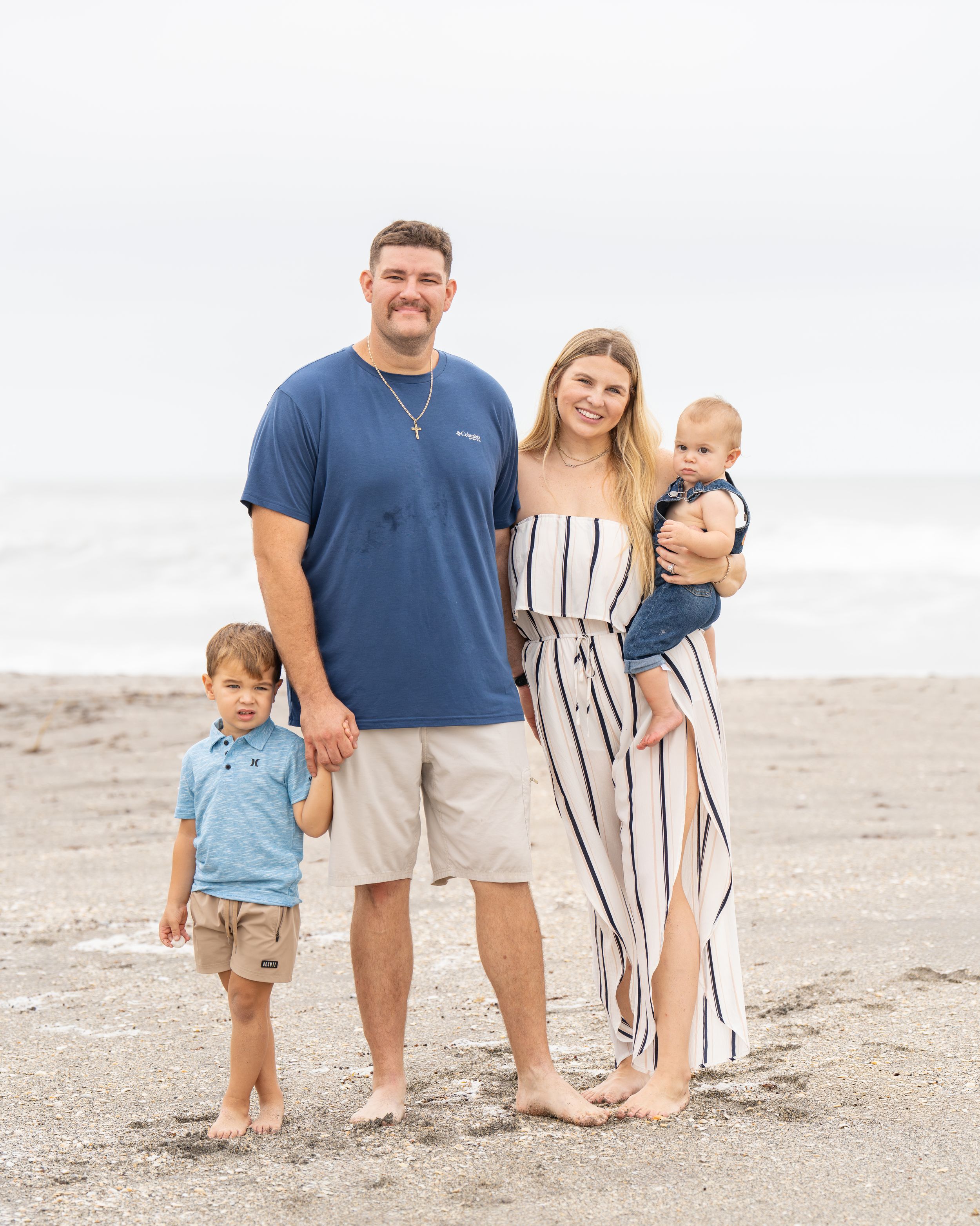Family enjoying a sunny day together walking on a sandy beach wearing coordinated blue and white outfits.