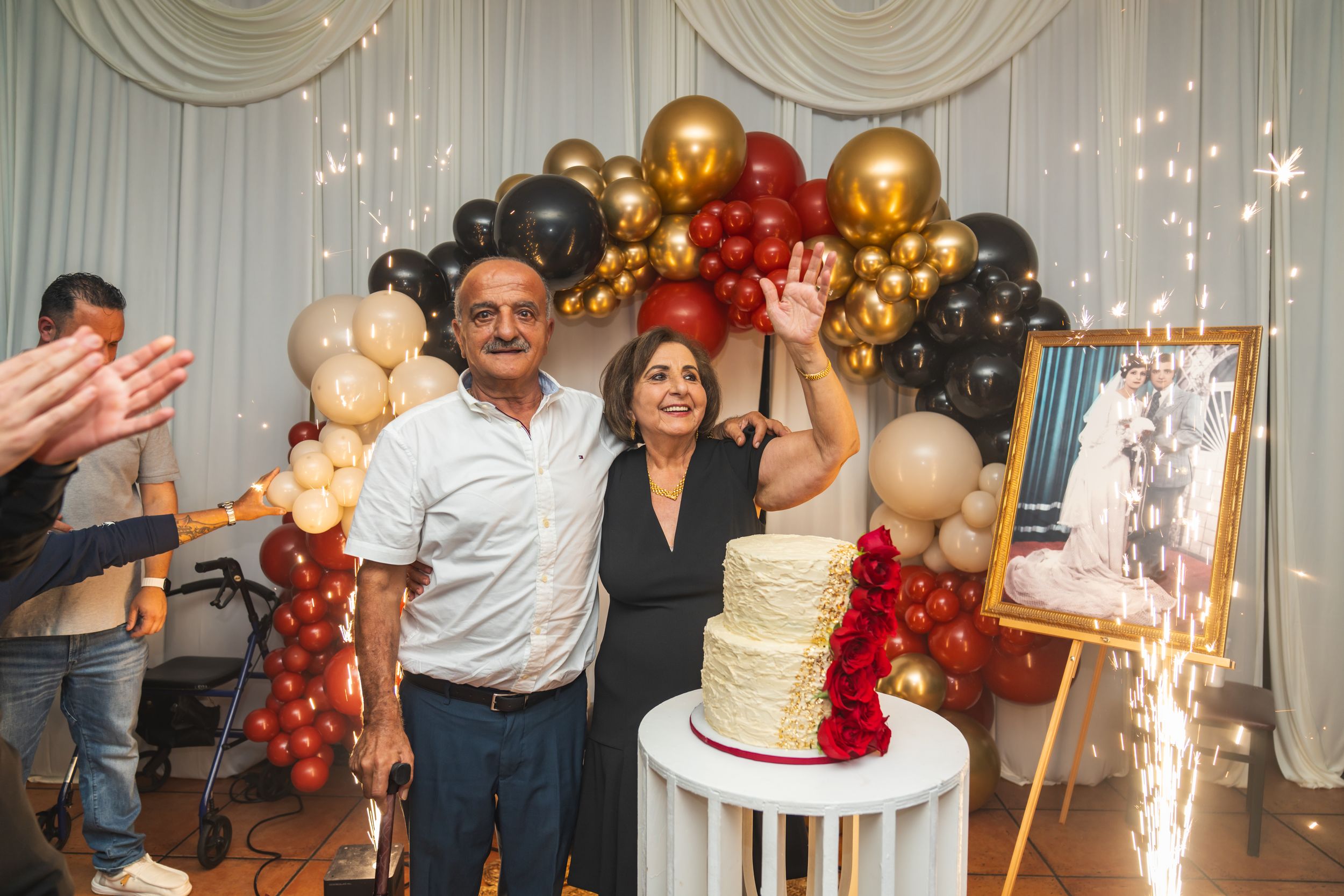 A festive celebration with balloon decorations, sparklers and a white tiered cake against an elegant backdrop.