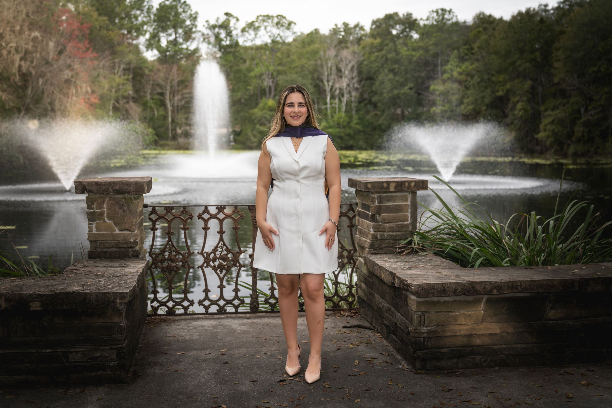A person in a white dress stands on stone steps with ornate fountains spraying water in a garden background.