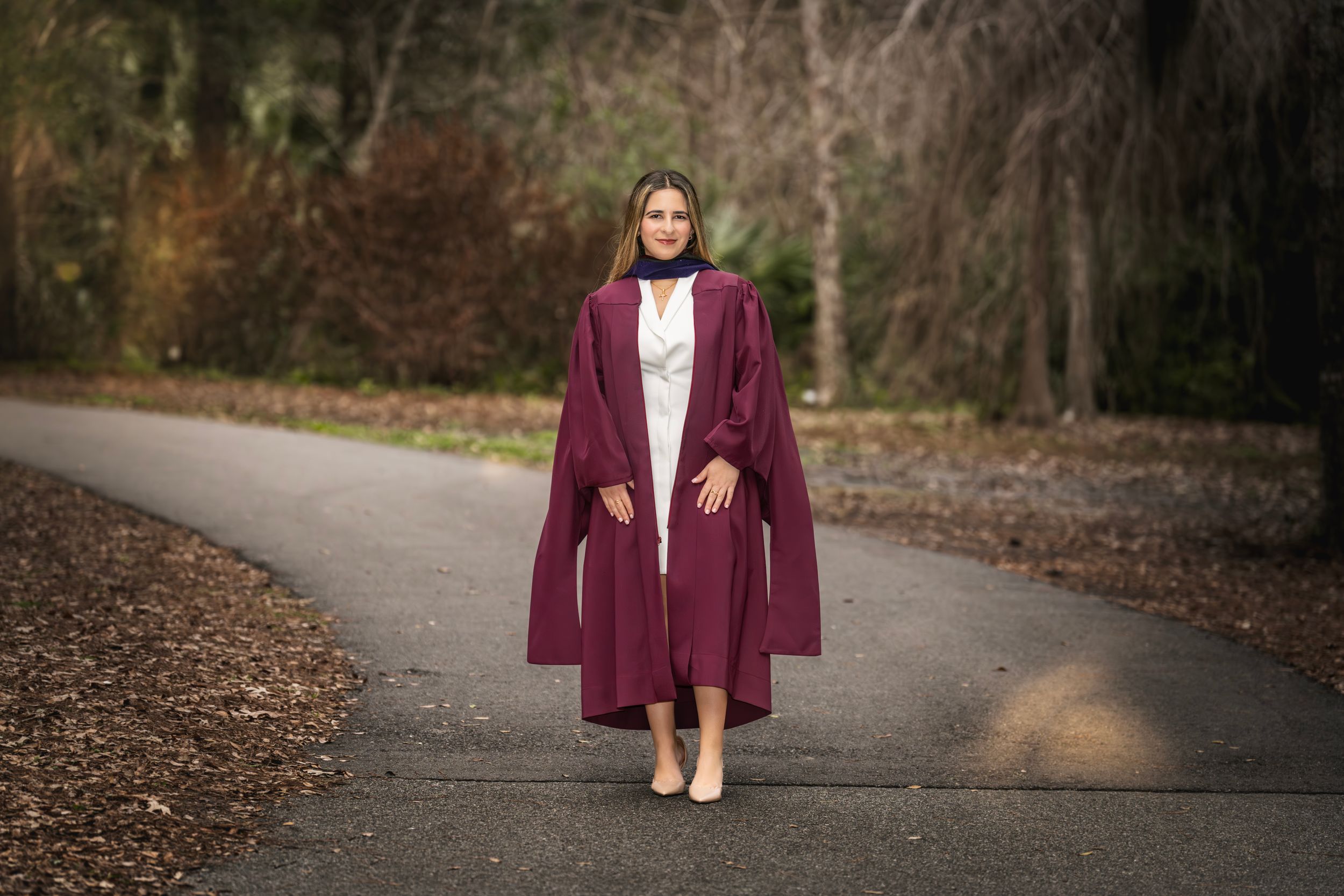 A person in a burgundy blazer and white shirt walks along a wooded path in autumn.