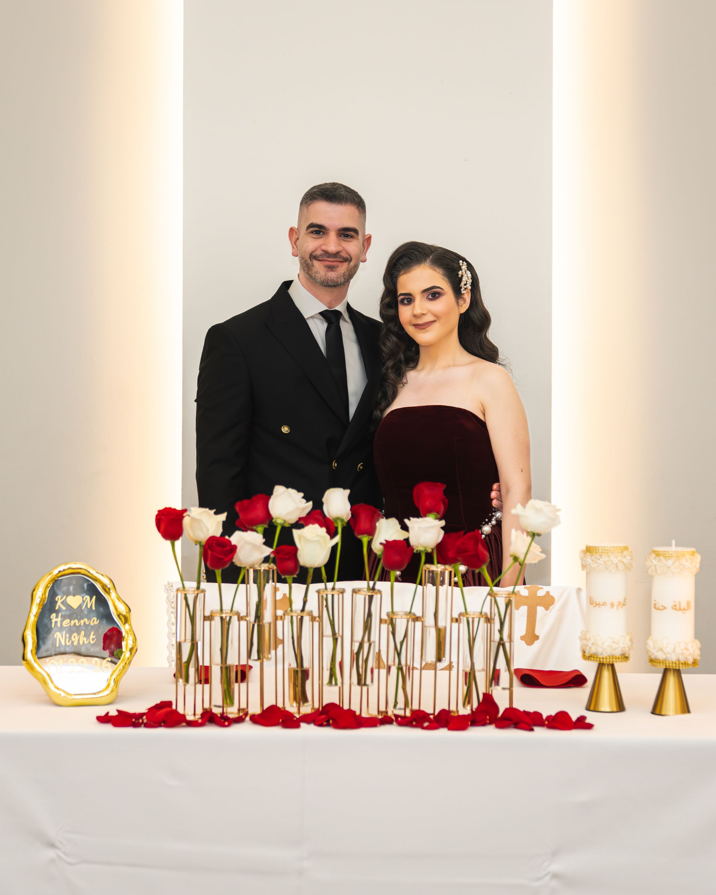 Elegant wedding reception table decor with red and white roses, gold candlesticks, and romantic candlelight on white tablecloth.