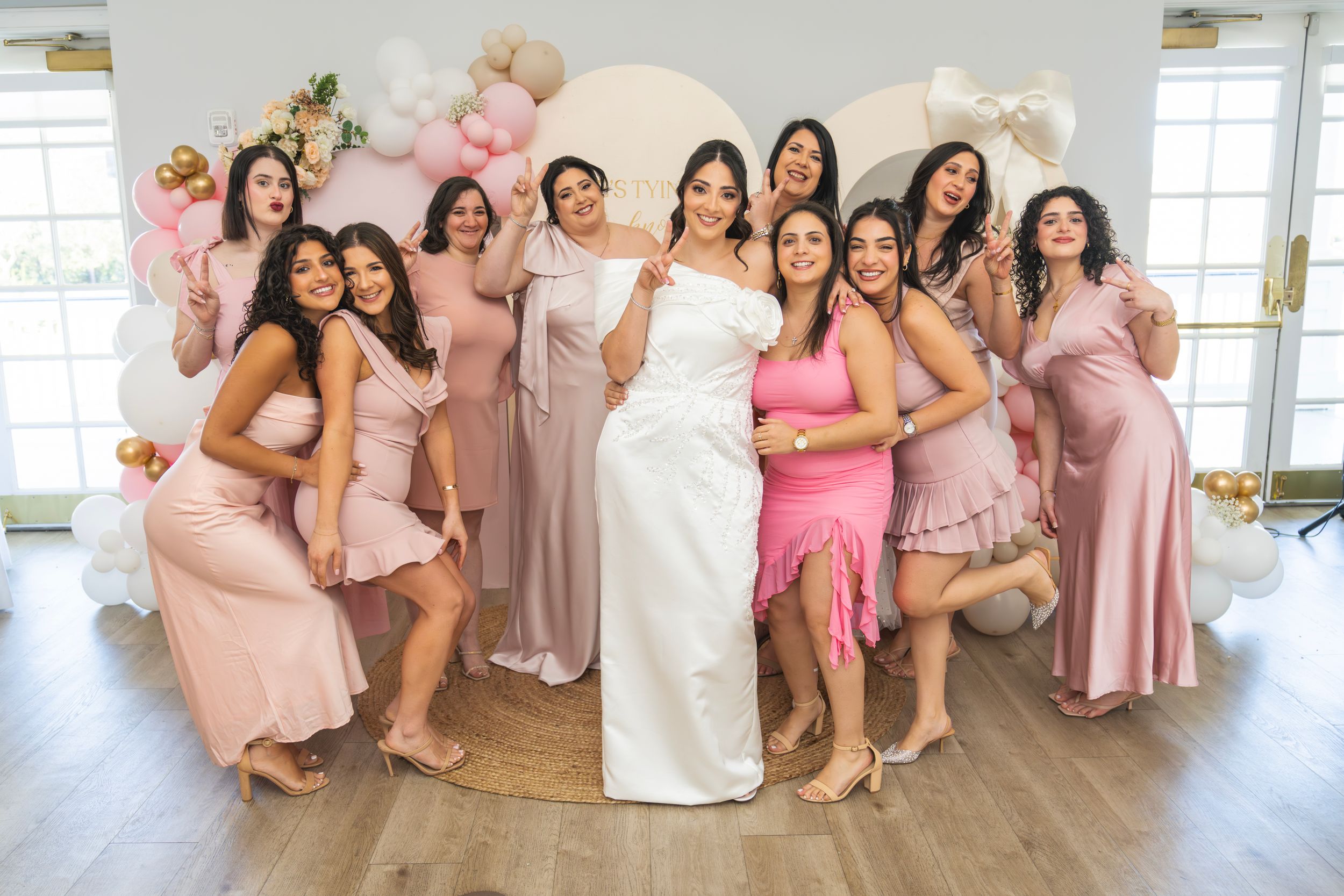 Bridesmaids in pink dresses pose together in a bright indoor setting during a wedding celebration.