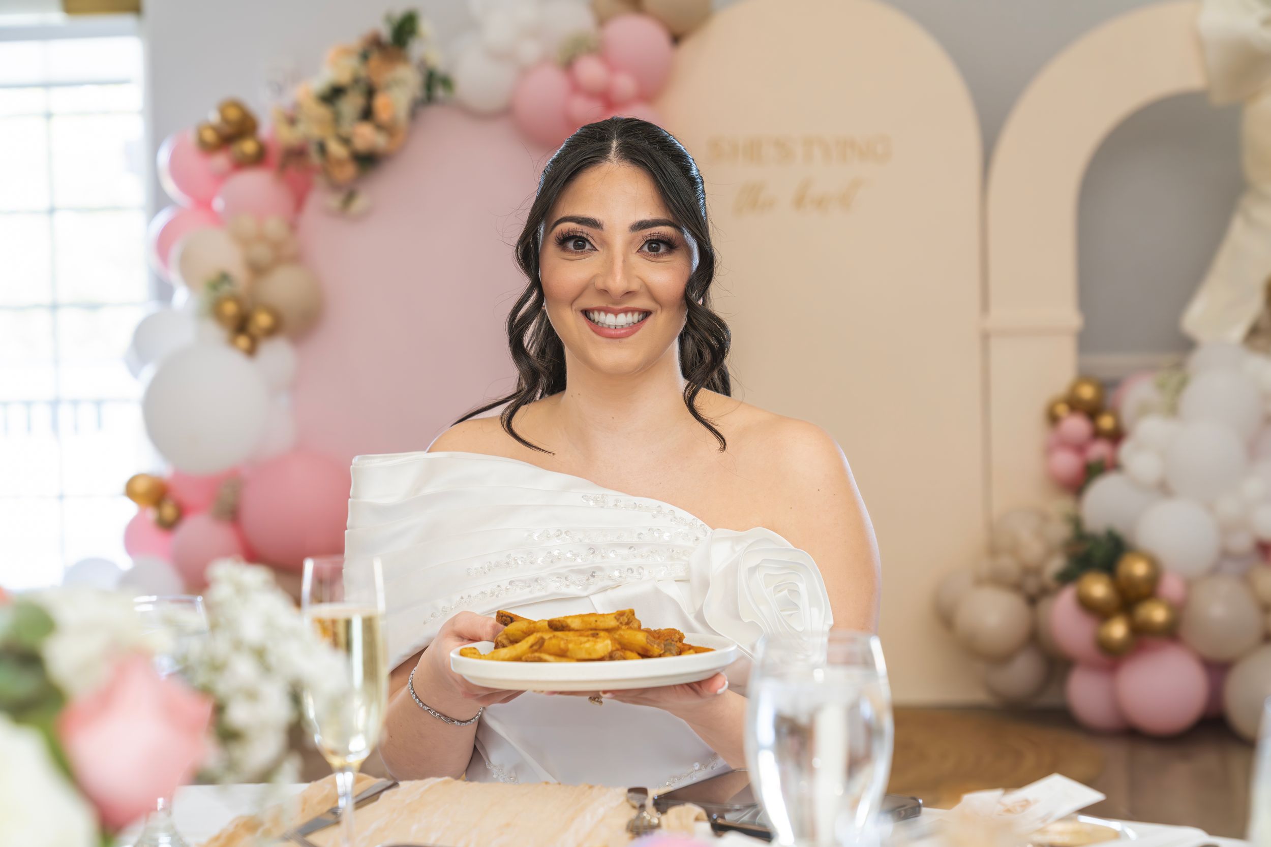 A festive wedding reception setup with pink balloons, floral arrangements, and elegant place settings at dining tables.