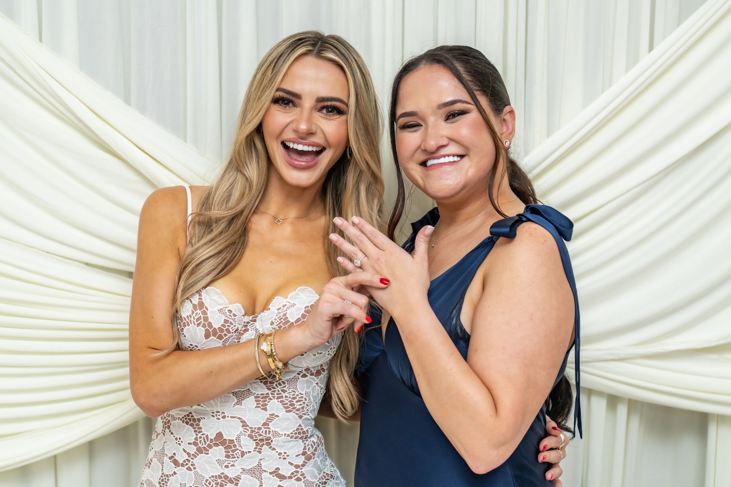 Two people in formal attire share a joyful moment together against a white draped backdrop.