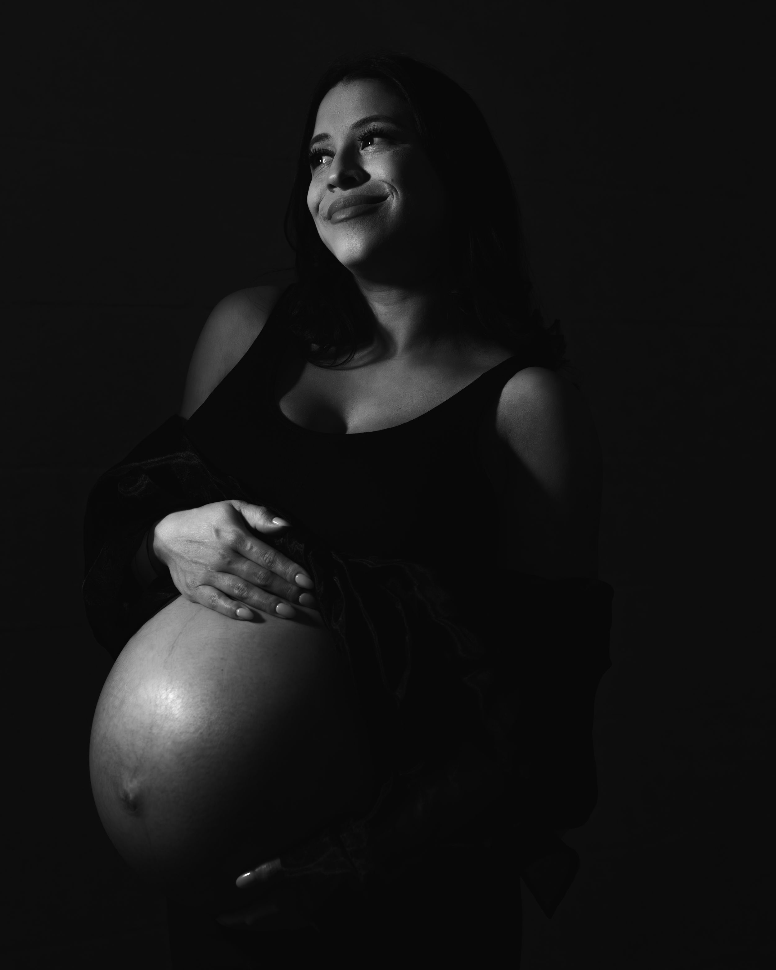 A series of artistic black and white maternity photos showing a pregnant belly in dramatic lighting and shadows.