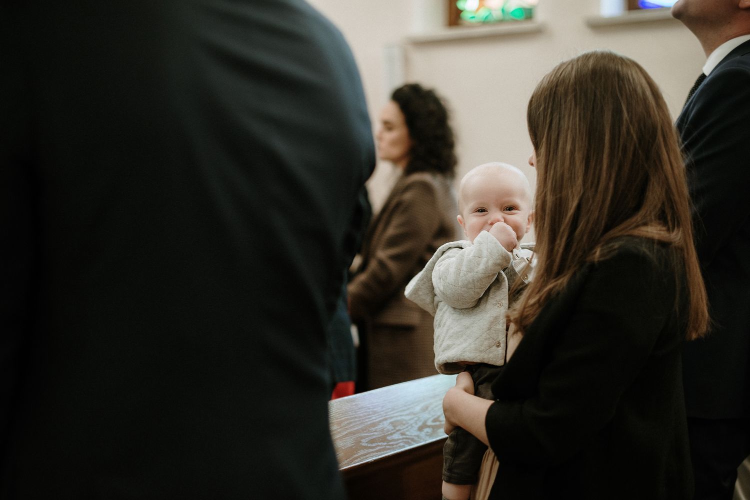 A small baby in a light colored outfit is held during what appears to be a church service or ceremony.