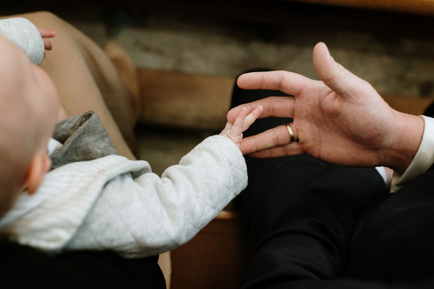 A small hand reaches out to touch an adult's hand wearing a wedding ring in an intimate moment.