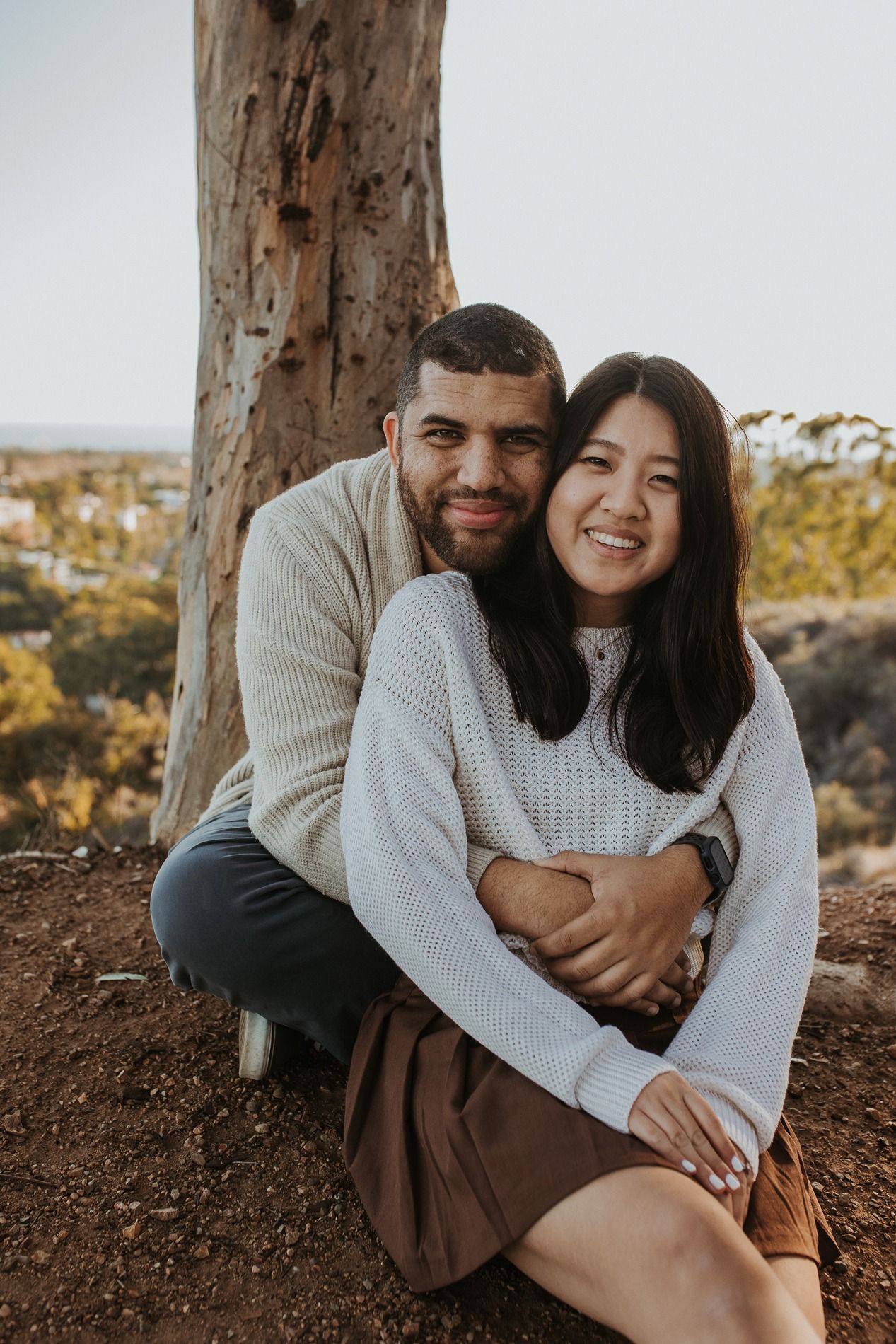 Couple sitting together under autumn trees in a park enjoying an intimate moment at Will Rogers State Park in the Palisades.