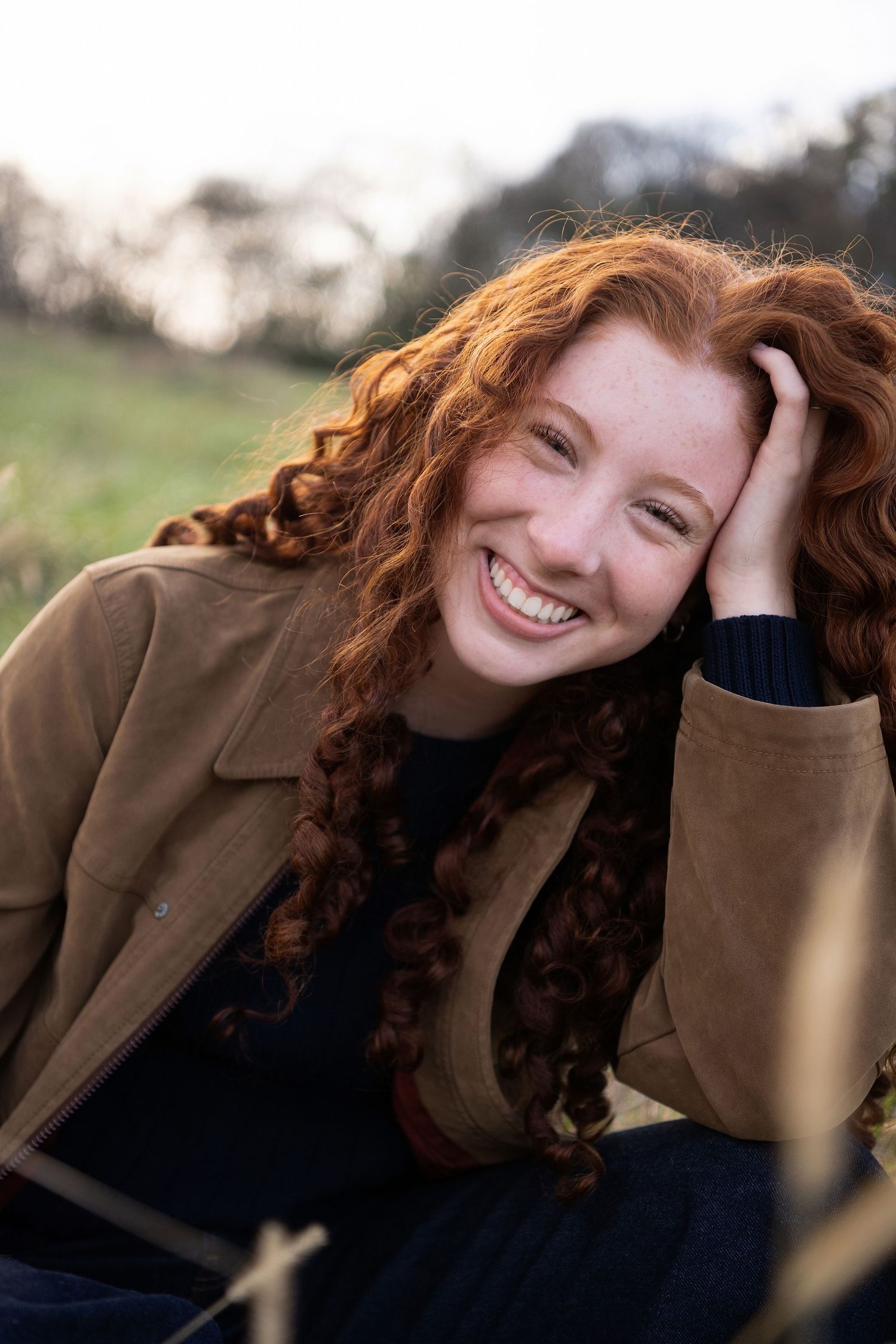 A series of candid outdoor portraits showing a person with curly red hair wearing a brown jacket against a natural background.