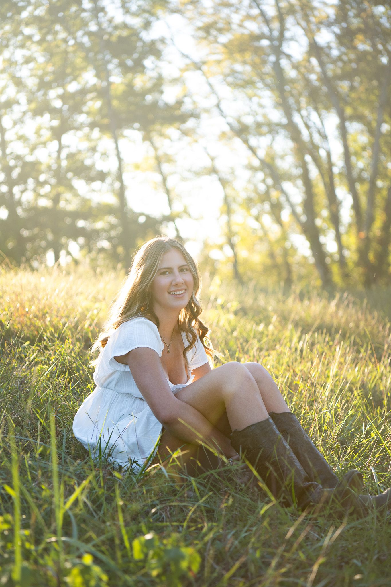 Relaxed person in white dress laying on grass in golden sunlit meadow during sunset.