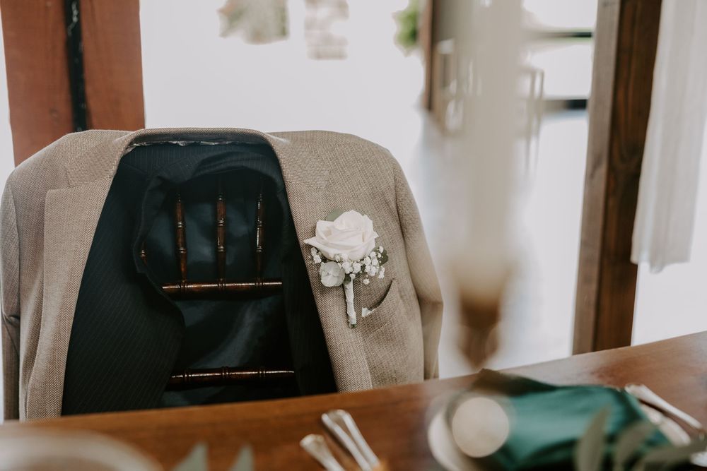 Groom's navy suit jacket with white floral boutonniere draped over a wooden chair at a wedding reception.