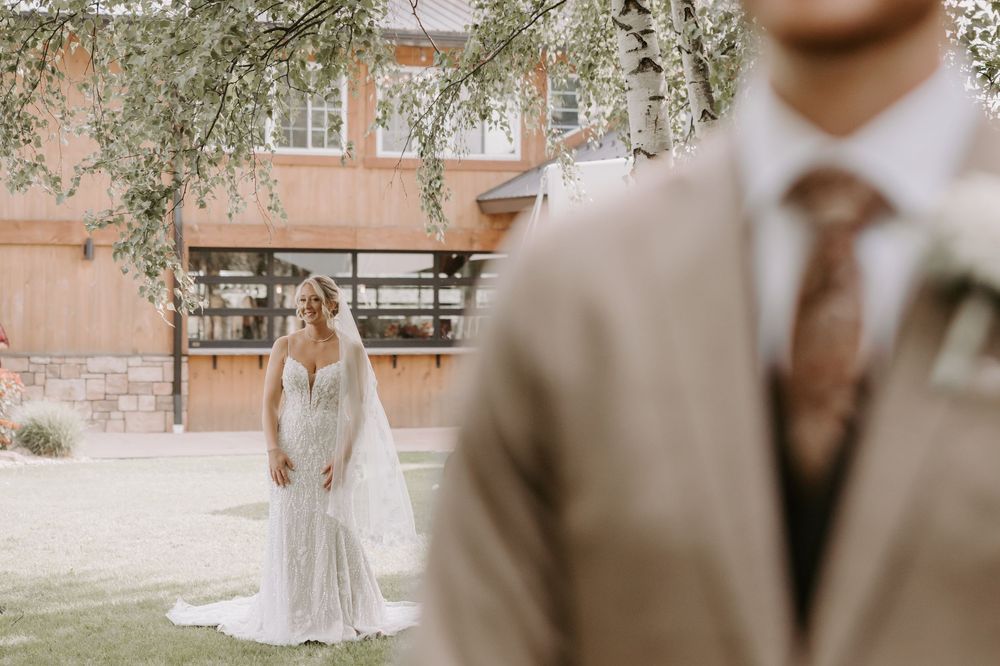 Bride in white lace gown with veil approaching groom in tan suit for first look.